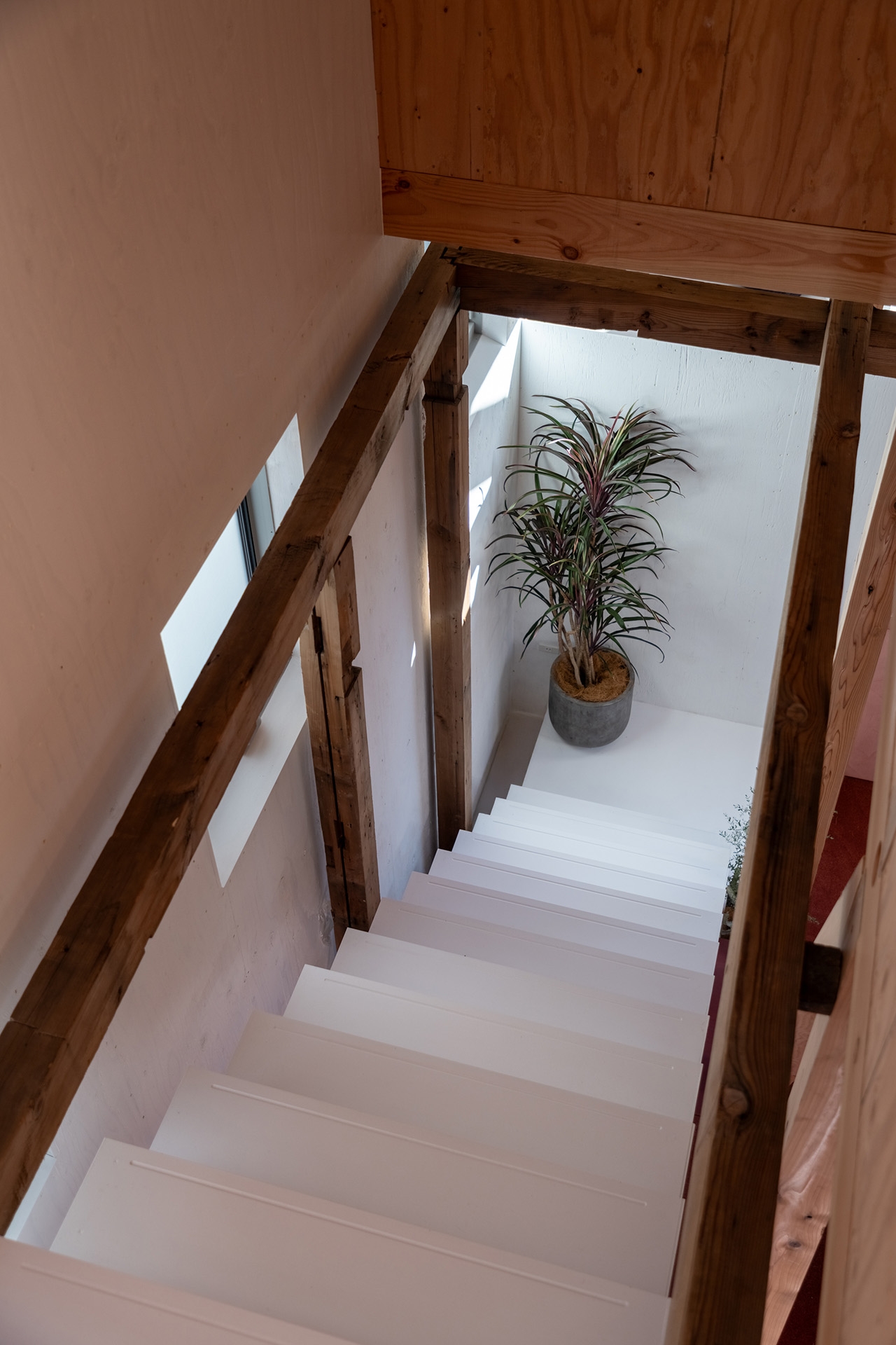 古材の梁や柱と白く意匠的な階段の対比 / 裏側は本棚に