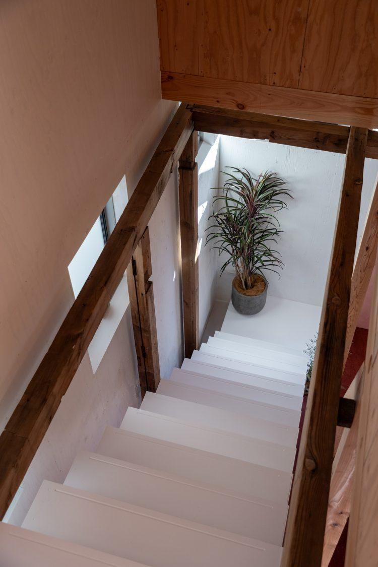 古材の梁や柱と白く意匠的な階段の対比 / 裏側は本棚に